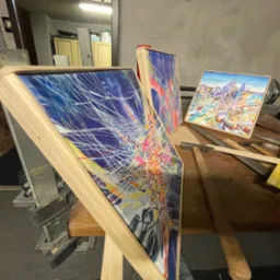 Trzy obrazy na drewnianych blejtramach, jeden w imadle, na stole z narzędziami, w warsztacie.