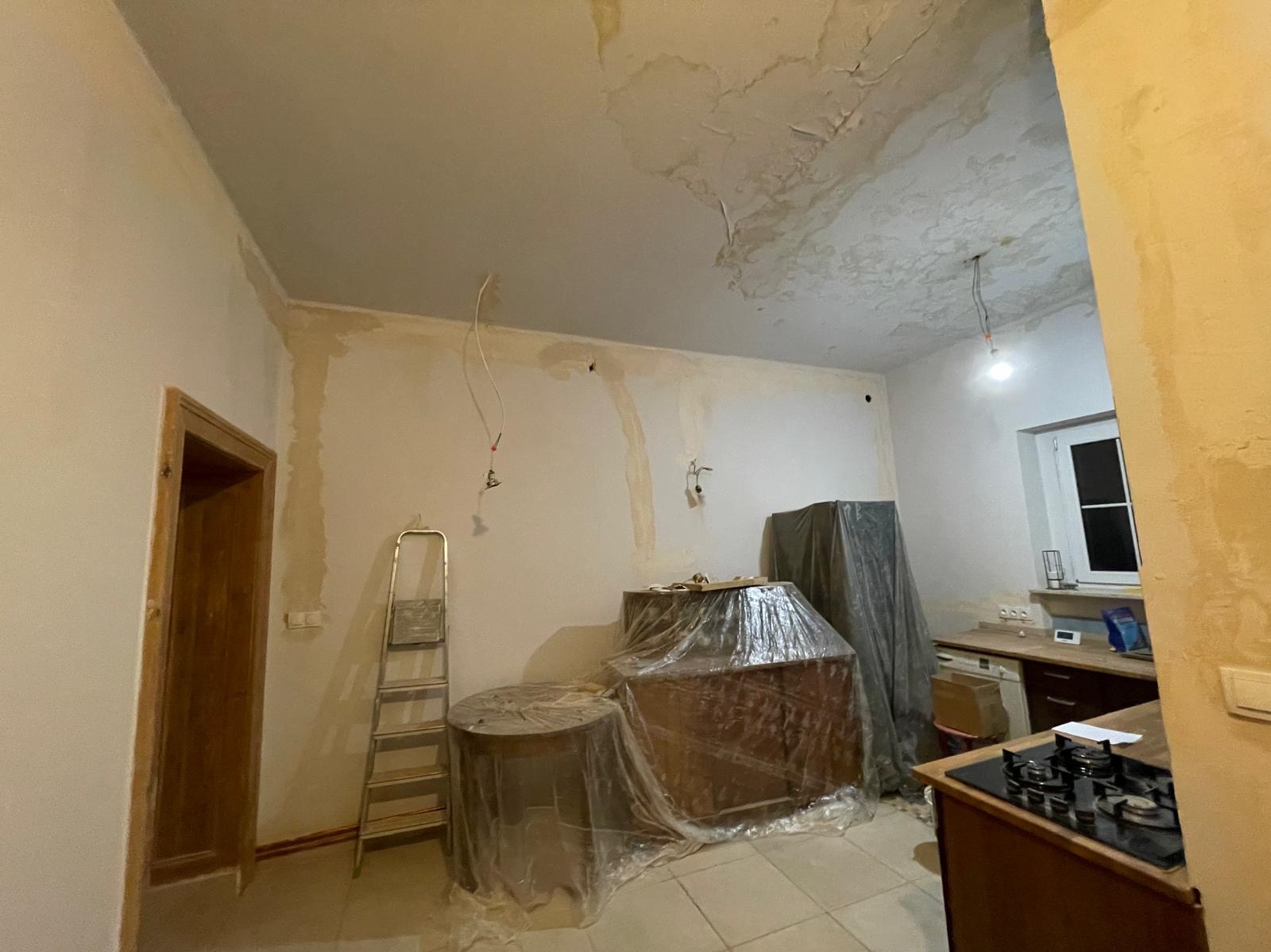 Wnętrze mieszkania w Bytomiu w trakcie przygotowań do prac wykończeniowych: zabezpieczone meble folią malarską, widoczna drabina i ślady po zalaniu na suficie.