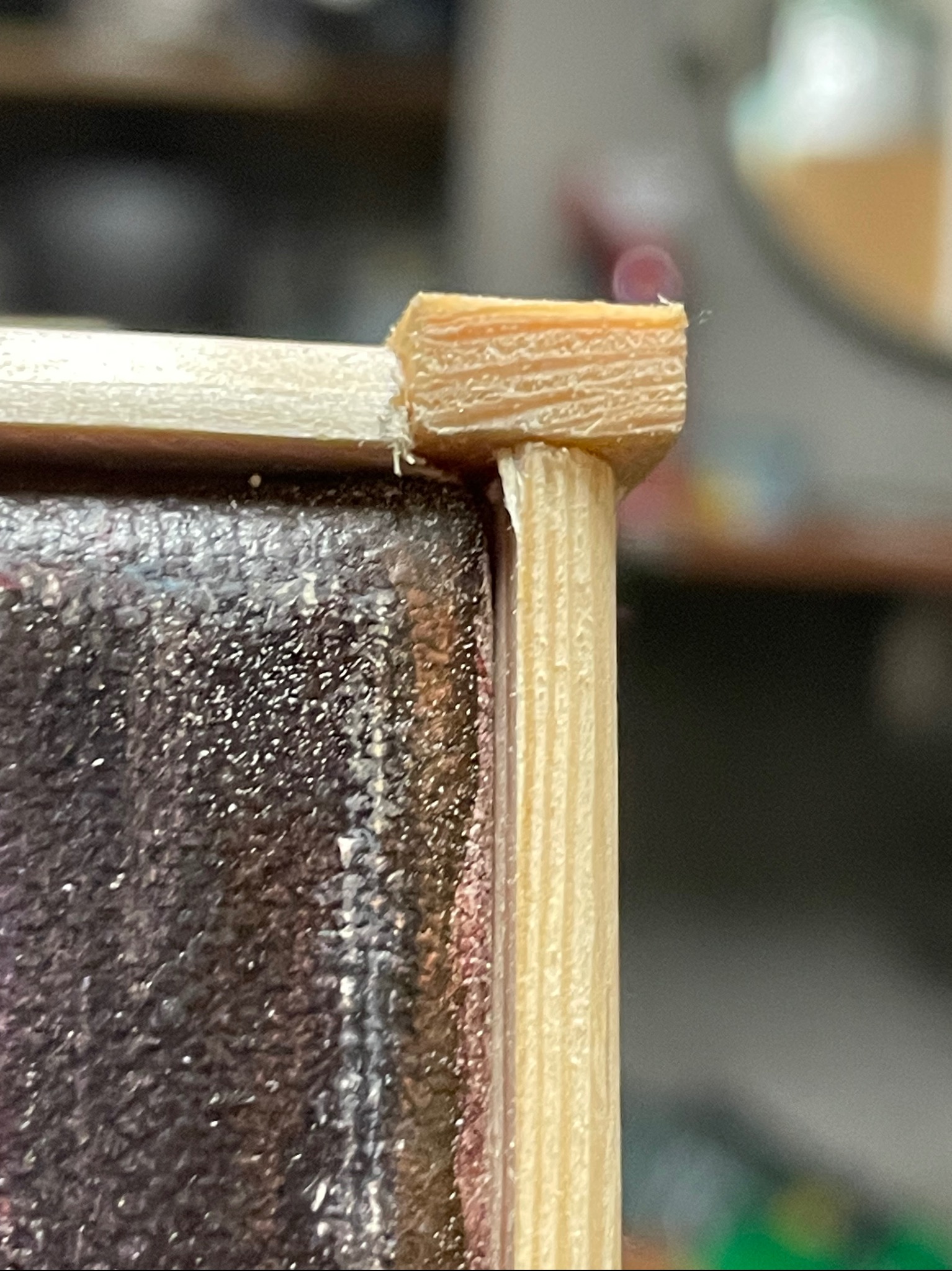 Detail of a wooden frame corner joint, showing a dowel and mitered edge, with visible glue residue.