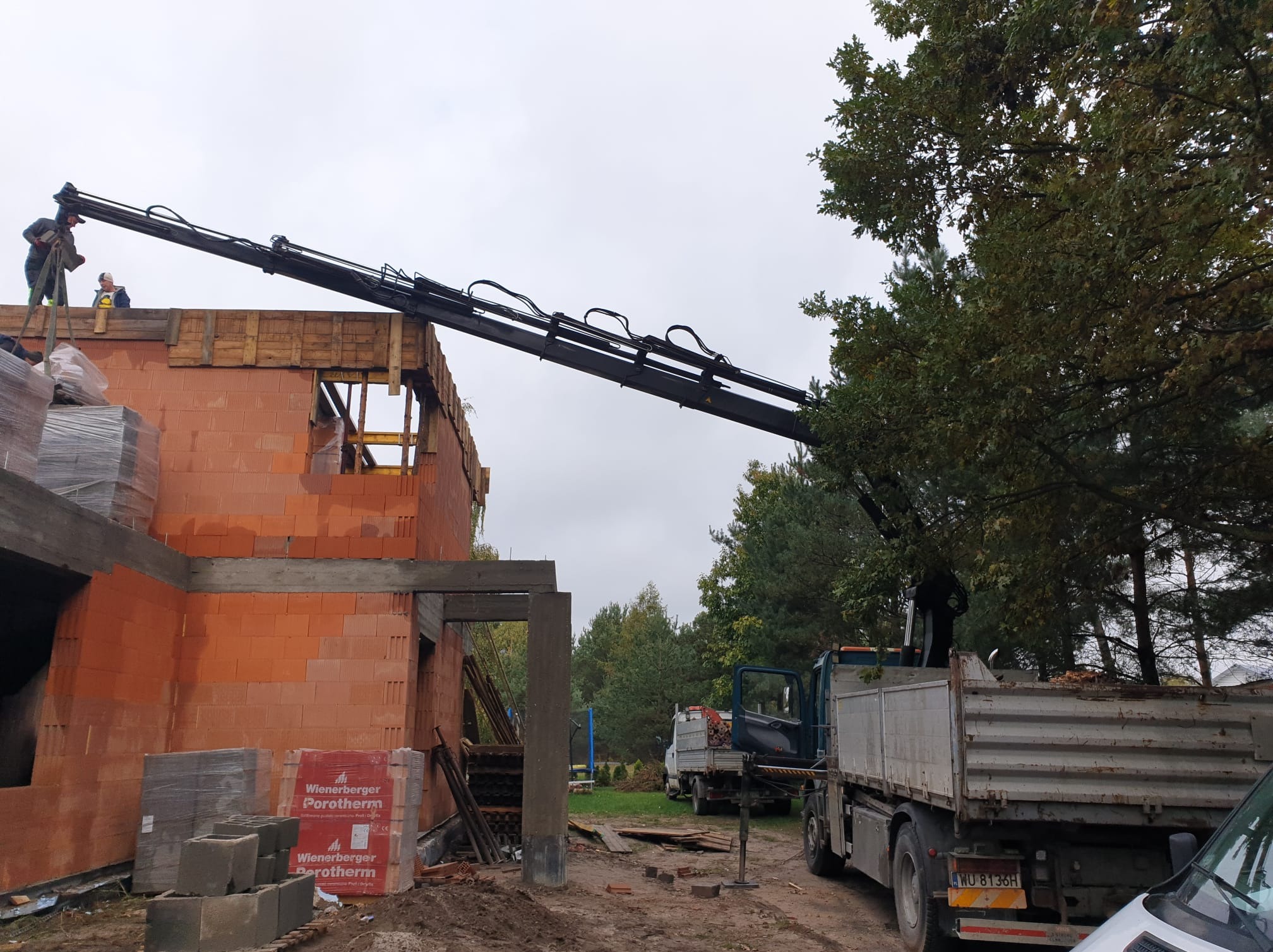 Budowa domu z czerwonej cegły Porotherm: dźwig samochodowy podaje materiały na strop, widoczni pracownicy na górze.