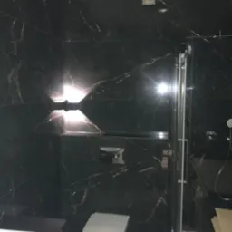 Nowoczesna łazienka z czarnymi płytkami imitującymi marmur, podświetlana ściana, wisząca toaleta i szklana kabina prysznicowa.