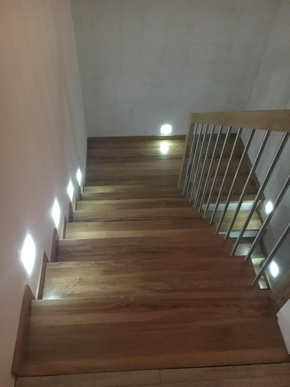 Drewniane schody z metalową balustradą oświetlone wbudowanymi lampami ściennymi, widok z góry.