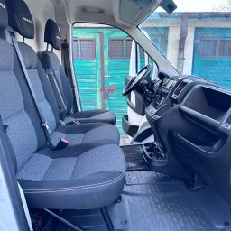 Dominik Ordowski Amber House - Wnętrze busa z trzema fotelami z szarej tapicerki i czarnymi zagłówkami, widok na deskę rozdzielczą i zielone drzwi garażowe w tle.