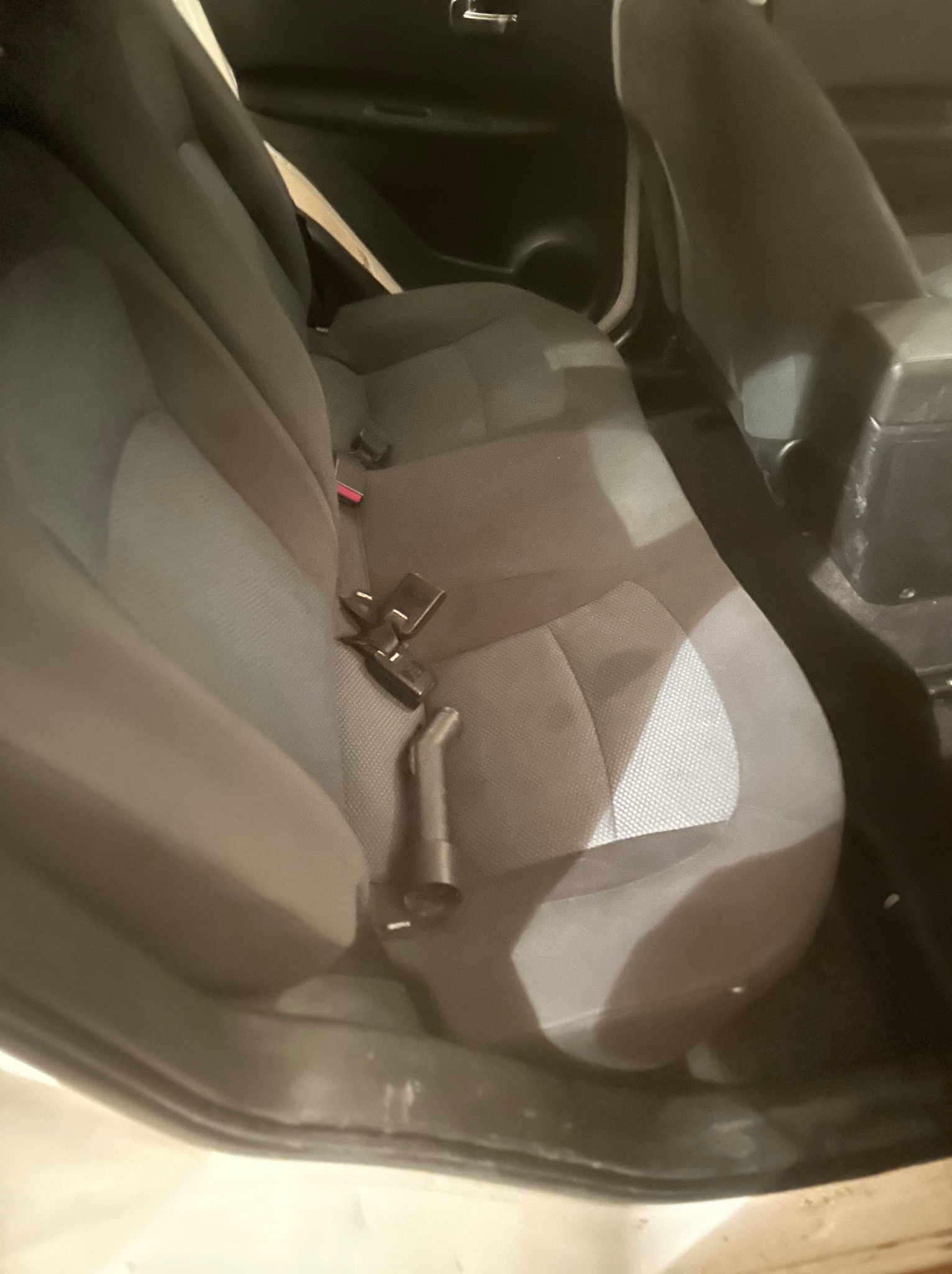 Wnętrze samochodu z widoczną tylną kanapą w odcieniach szarości, na której leży końcówka odkurzacza, prawdopodobnie w trakcie czyszczenia.