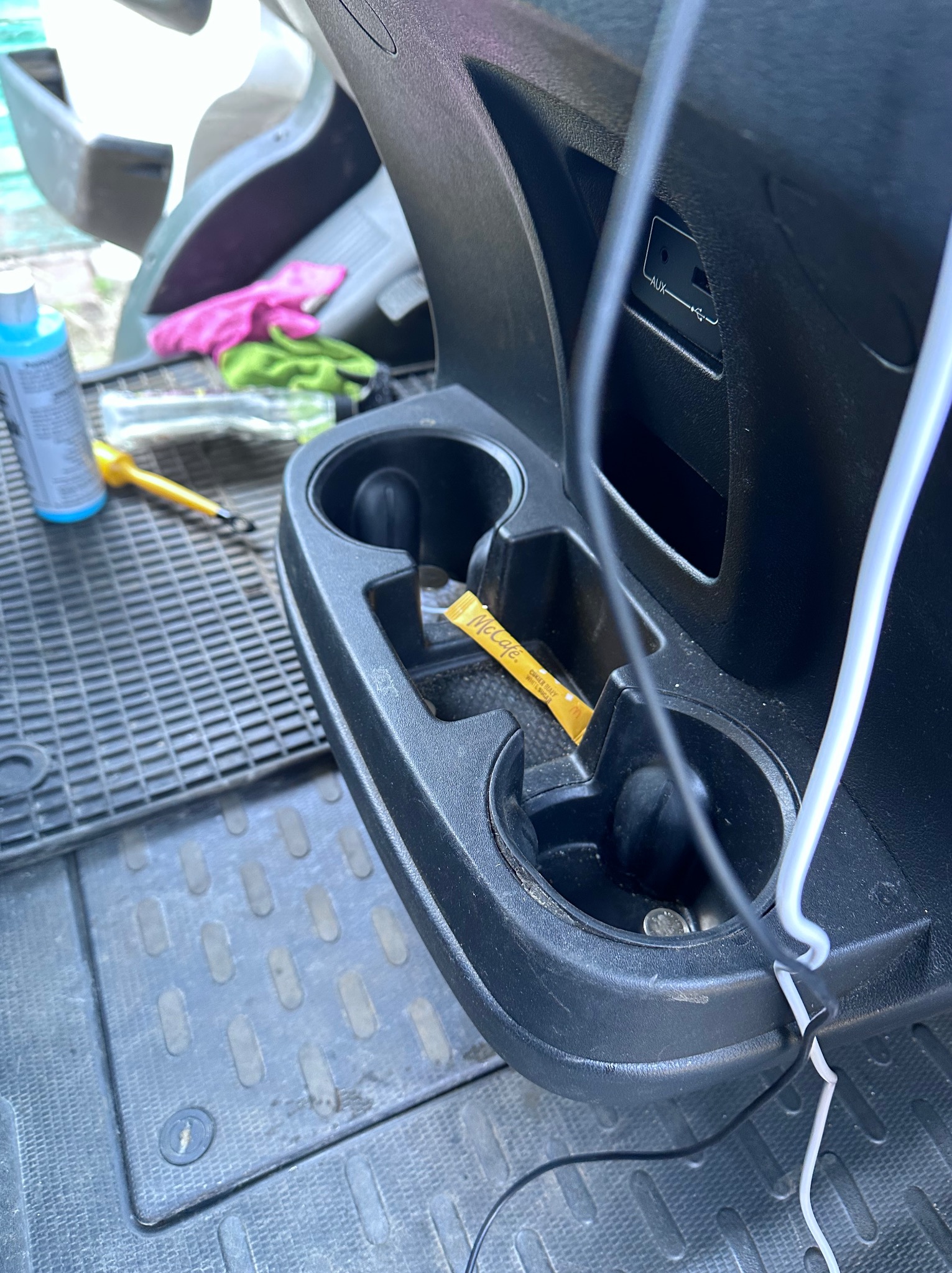 Wnętrze pojazdu przed praniem: widoczne zabrudzenia w uchwycie na napoje, kabel USB, płyn czyszczący i ściereczki w tle. Stan przed czyszczeniem tapicerki.