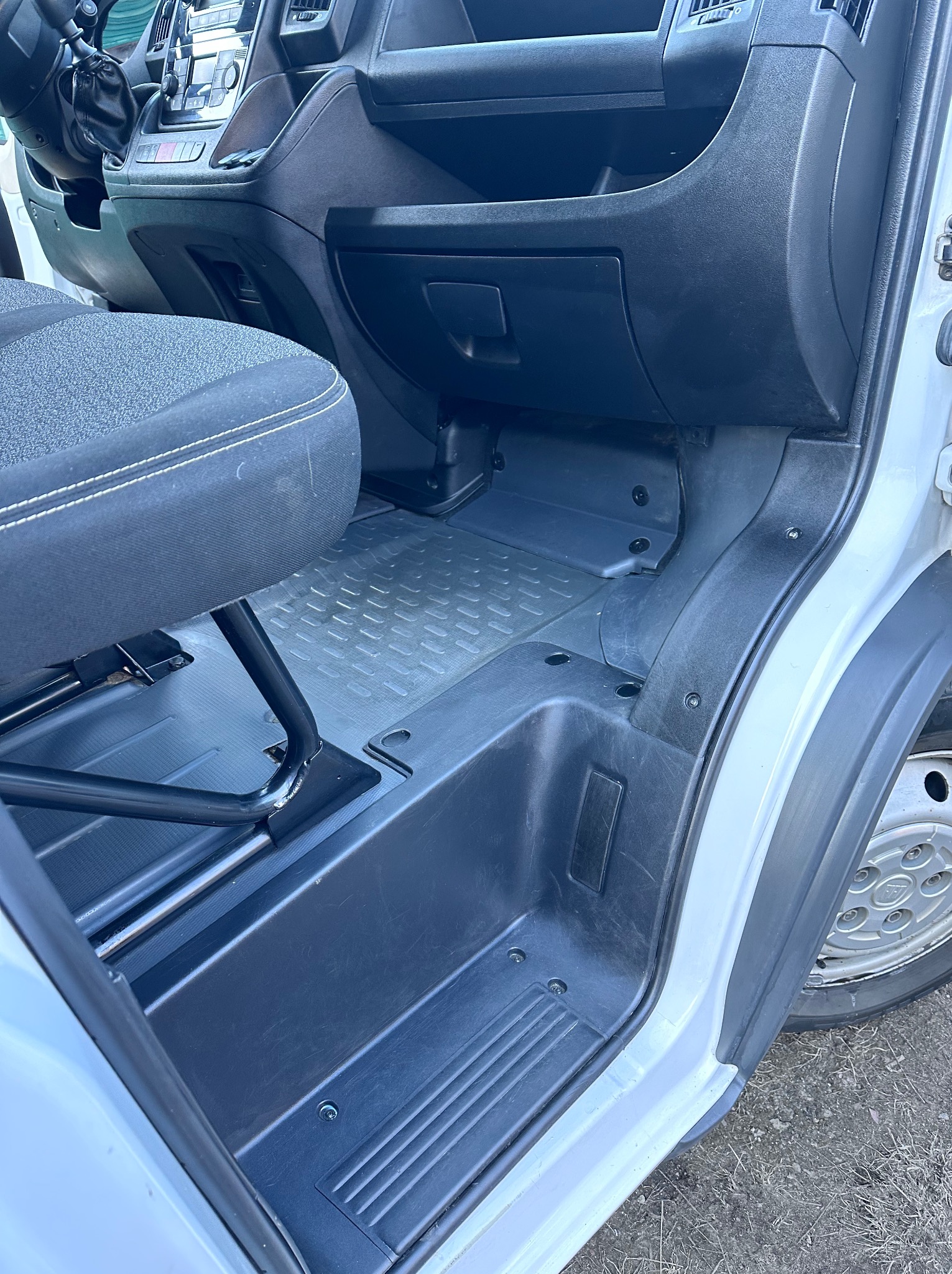 Wnętrze busa: czarna tapicerka fotela z białym szwem, szara podłoga z fakturą, czarne elementy plastikowe. Widoczny fragment koła. Ujęcie od dołu, z bliska.