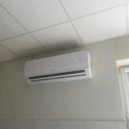 Mateusz Góral - Biały klimatyzator marki Sevra zamontowany na ścianie z kafelkami, widoczny wyświetlacz z temperaturą 16 stopni, sufit kasetonowy w tle.