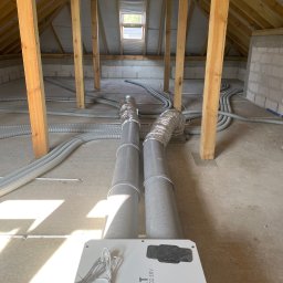 Mateusz Góral - Montaż rekuperatora REQNET izzi H.302 ERV na poddaszu z widocznymi przewodami wentylacyjnymi i drewnianą konstrukcją dachu.