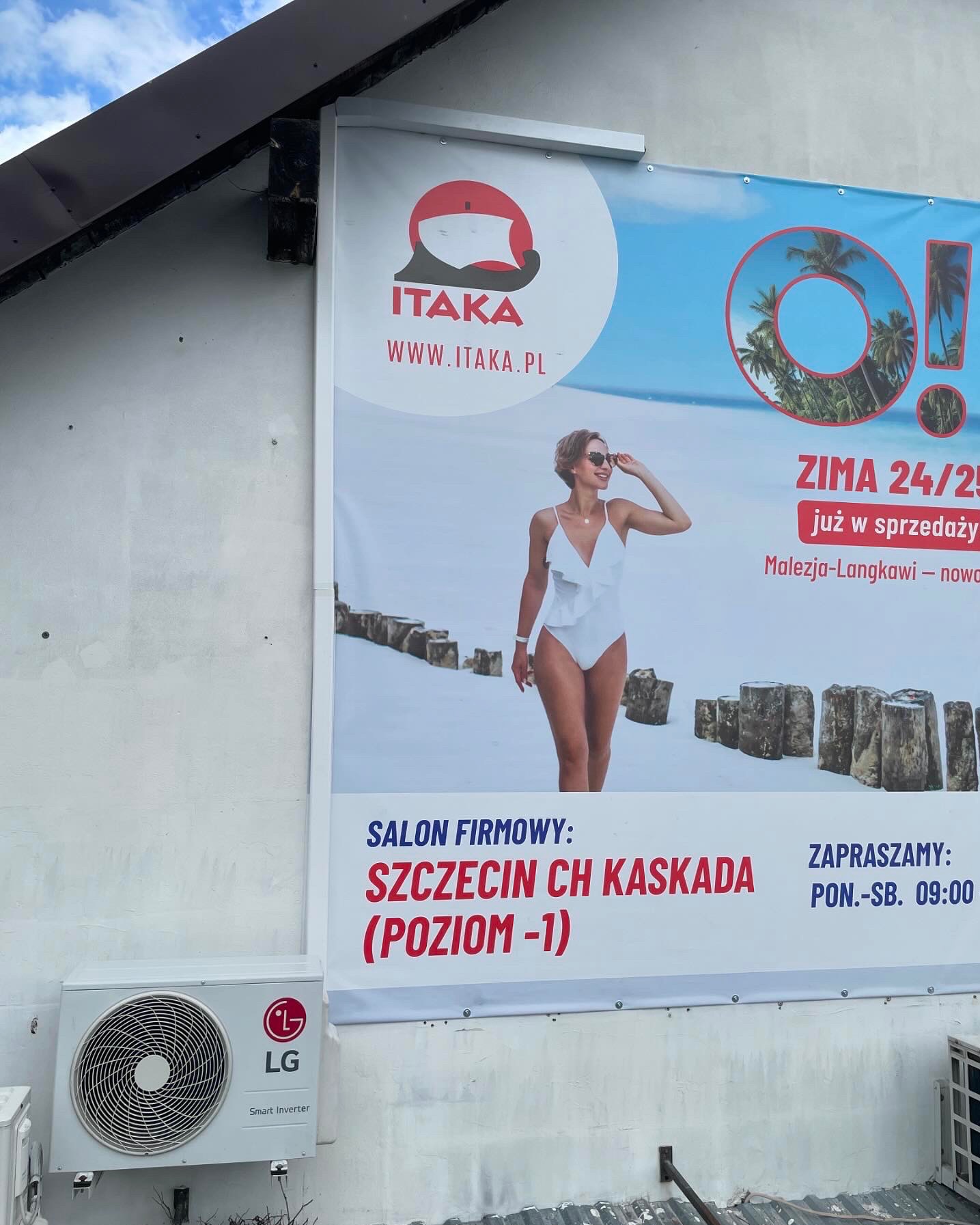 Zewnętrzna jednostka klimatyzacji LG zamontowana pod banerem reklamowym biura podróży Itaka, z ofertą zimowych wyjazdów do Malezji-Langkawi.