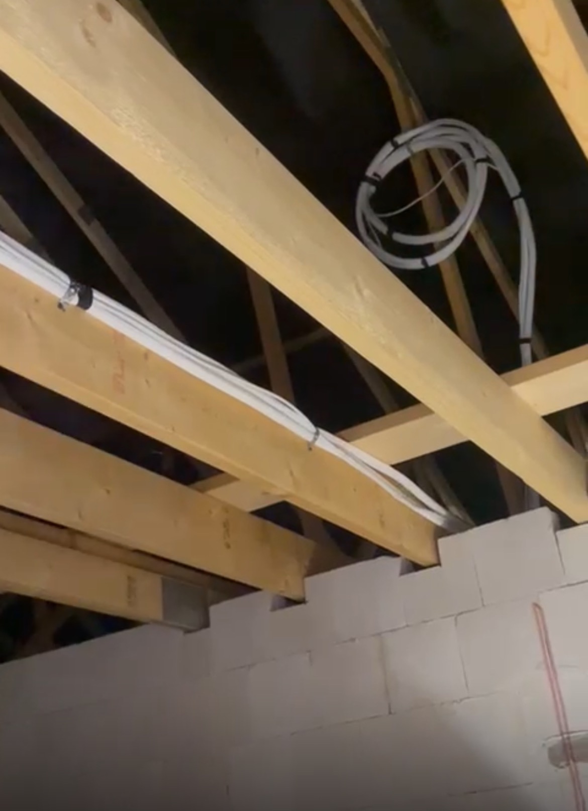 Białe przewody instalacji wentylacyjnej przymocowane do drewnianych belek stropowych w surowym wnętrzu budynku z białymi ścianami z betonu komórkowego.