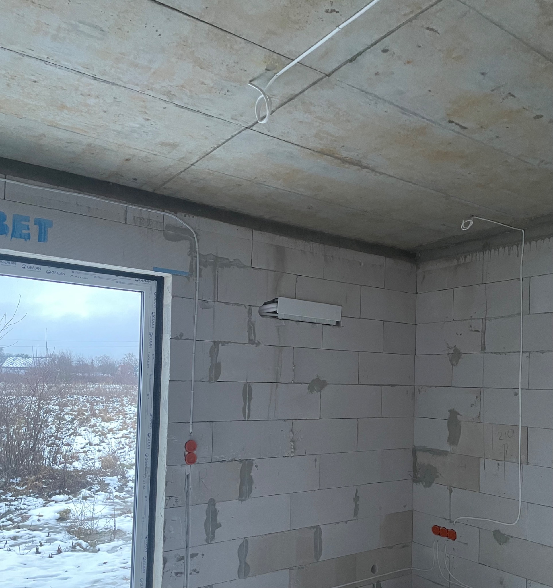 Surowy stan wnętrza domu w trakcie instalacji przewodów wentylacyjnych i elektrycznych, widoczne otwory wentylacyjne w ścianie z betonu komórkowego oraz wyprowadzone kable elektryczne i puszki...