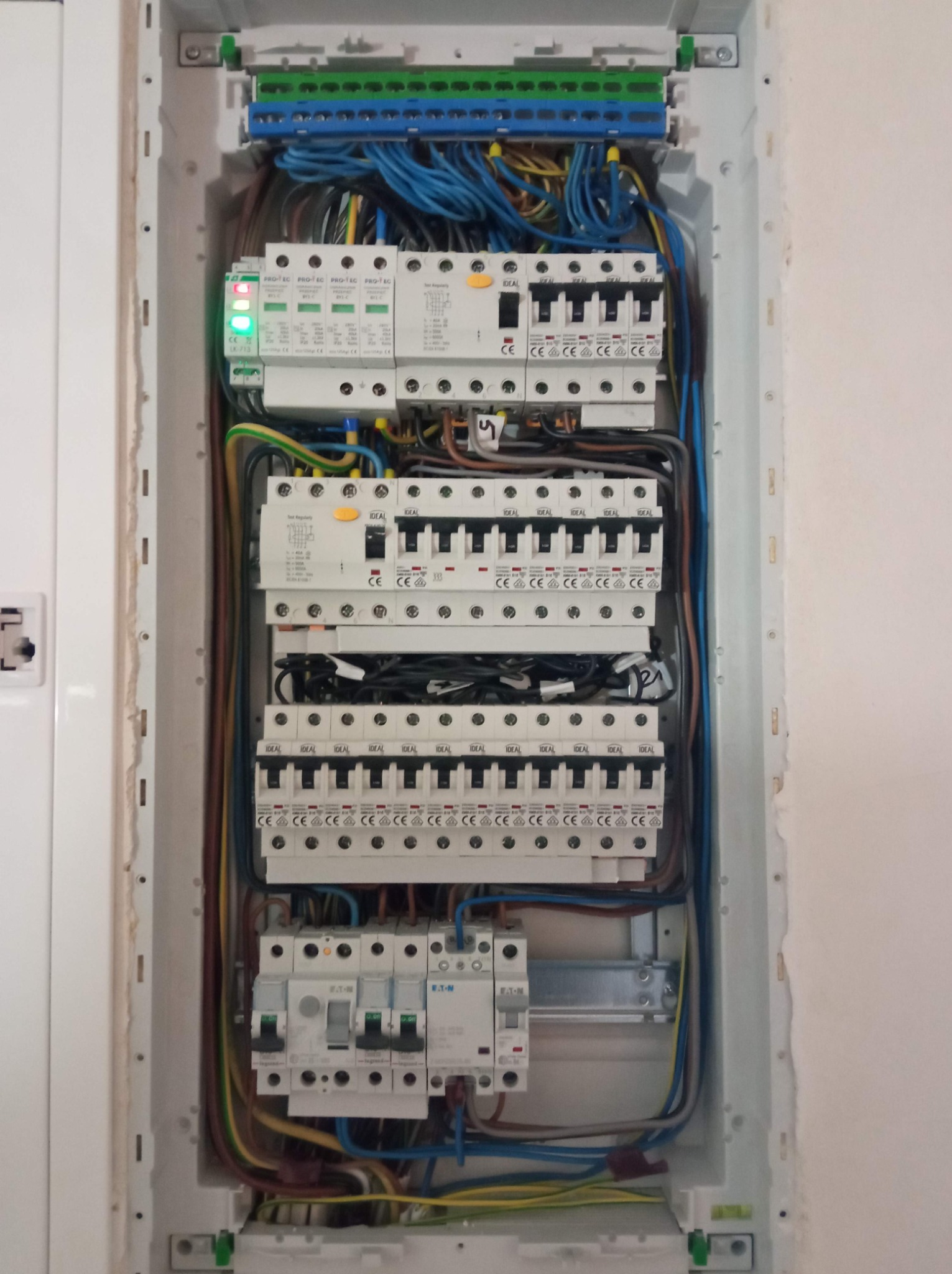 Rozdzielnica elektryczna wnękowa z zamontowanymi zabezpieczeniami nadprądowymi, ochronnikami przepięć i okablowaniem. Widoczne przewody w różnych kolorach oraz aparatura modułowa firm IDEAL i EATON.