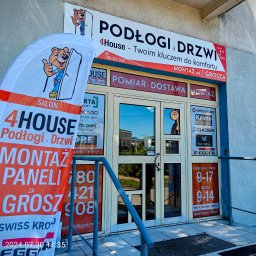 4HOUSE PODŁOGI DRZWI SPÓŁKA Z OGRANICZONĄ ODPOWIEDZIALNOŚCIĄ - Fasada salonu 4House z reklamami podłóg i drzwi, widoczny baner z napisem 'Montaż paneli za 1 grosz', oklejone okna z ofertą i logotypami producentów.