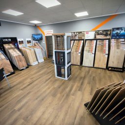 4HOUSE PODŁOGI DRZWI SPÓŁKA Z OGRANICZONĄ ODPOWIEDZIALNOŚCIĄ - Salon z ekspozycją paneli podłogowych różnych marek i wzorów, prezentowanych na stojakach i ścianach, w jasnym wnętrzu z oświetleniem sufitowym.