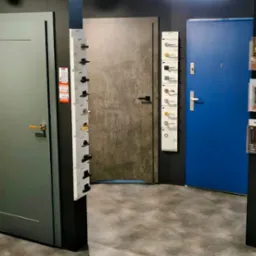 Ekspozycja różnorodnych drzwi wewnętrznych i zewnętrznych w salonie, z katalogami klamek i okuć, ukazująca szeroki wybór wzorów i kolorów.