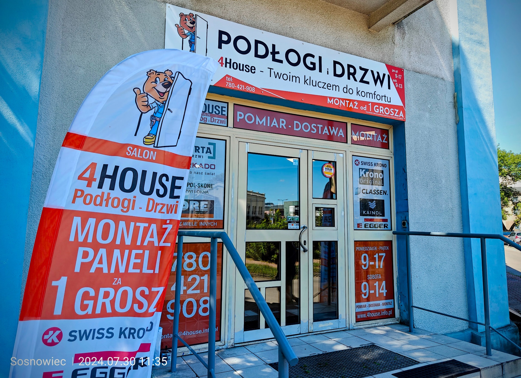 Fasada salonu 4House z reklamami podłóg i drzwi, widoczny baner z napisem 'Montaż paneli za 1 grosz', oklejone okna z ofertą i logotypami producentów.
