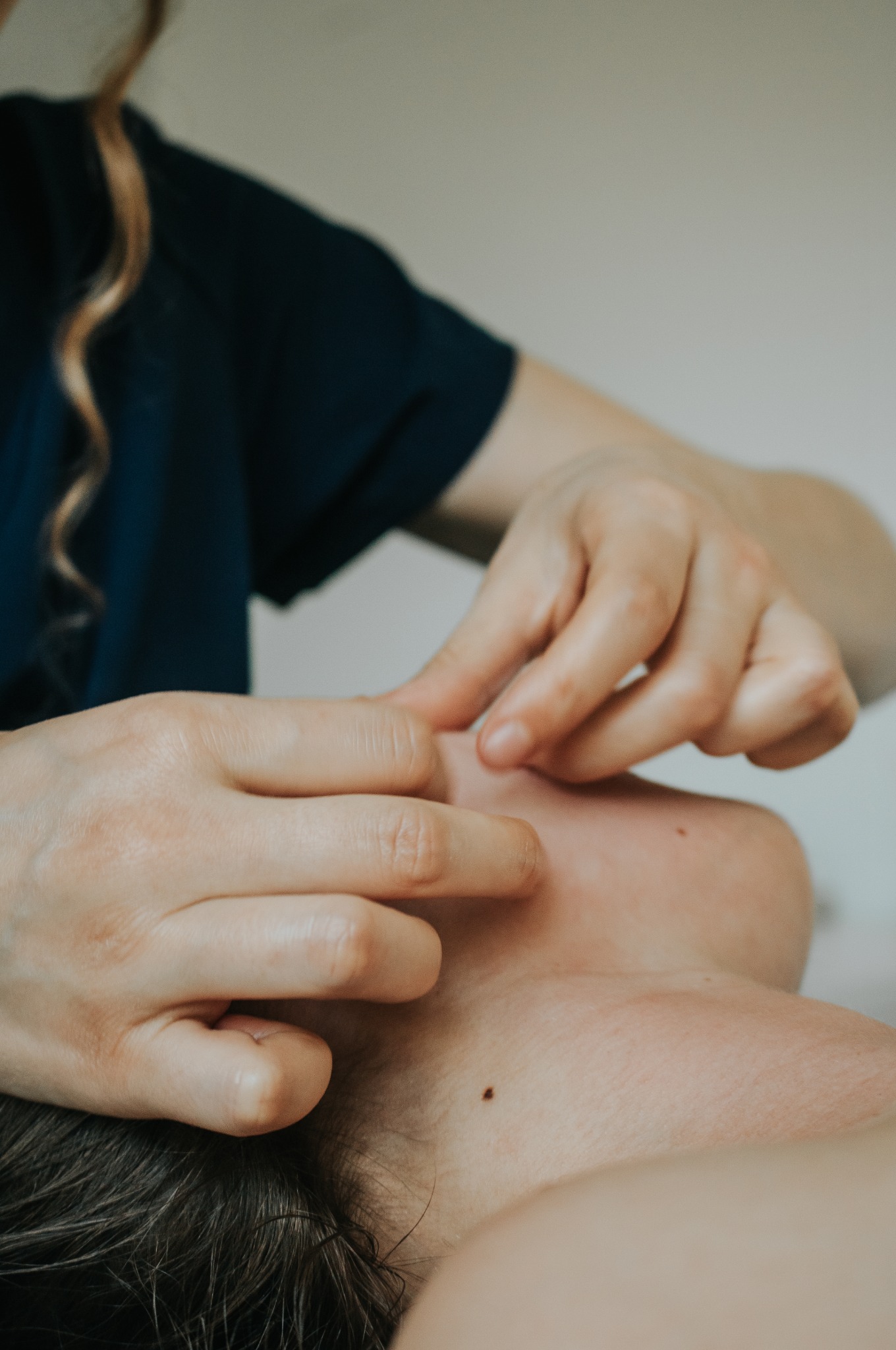 Terapeuta manualnie stymuluje skórę twarzy kobiety, skupiając się na okolicy oka i policzka, widoczny pieprzyk na szyi.