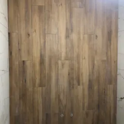 Ściana w łazience wyłożona podłużnymi płytkami imitującymi drewno, z widocznymi dwoma chromowanymi elementami instalacji, sąsiadująca z białą ścianą wyłożoną marmurkowymi płytkami.