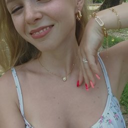 Angelikakuscontent - Uśmiechnięta blondynka z piegami prezentuje złotą biżuterię: kolczyki koła z perłami, naszyjnik z okrągłą zawieszką, bransoletki z różnymi ogniwami i pierścionki na palcu, z manicure w odcieniach...