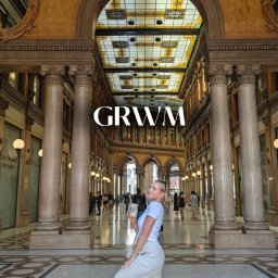 Angelikakuscontent - Kobieta pozuje w galerii handlowej z kolumnami, trzymając napój. Nałożony napis GRWM.