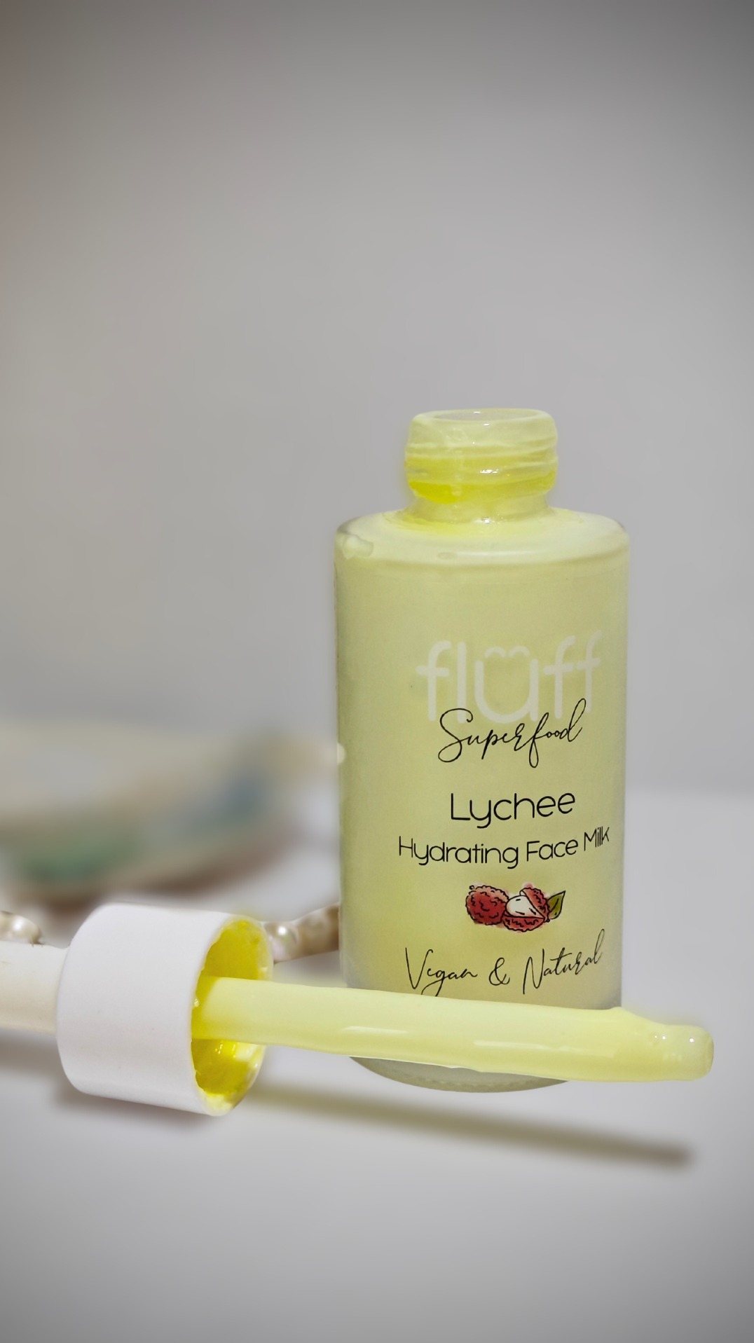 Butelka z mleczkiem do twarzy o zapachu liczi z pipetą, na rozmytym tle widać perły.