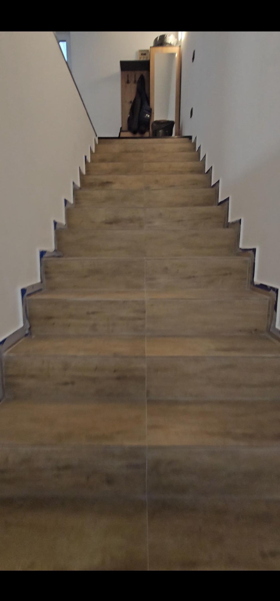 Schody wyłożone panelami imitującymi drewno, zabezpieczone taśmą malarską na krawędziach, widok od dołu.