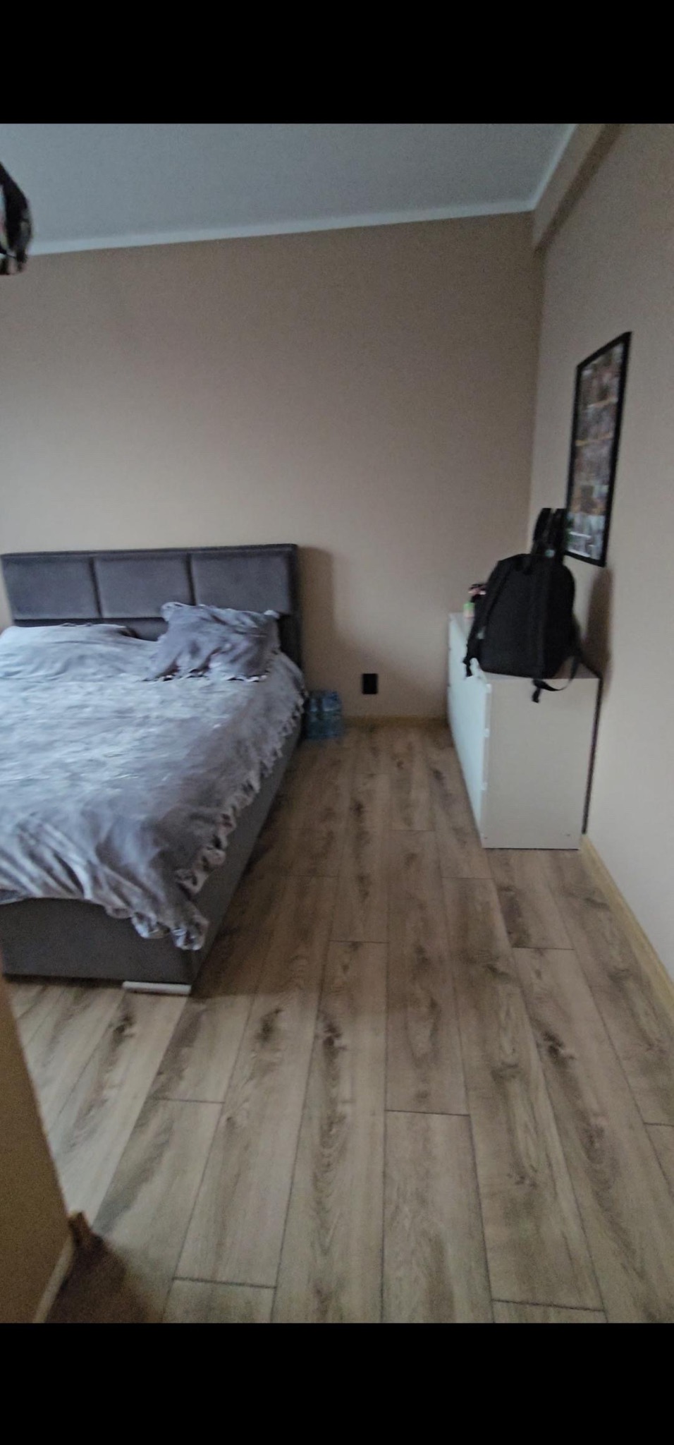 Jasne panele podłogowe ułożone w sypialni w Warszawie, widoczny fragment łóżka i szafki nocnej z plecakiem.