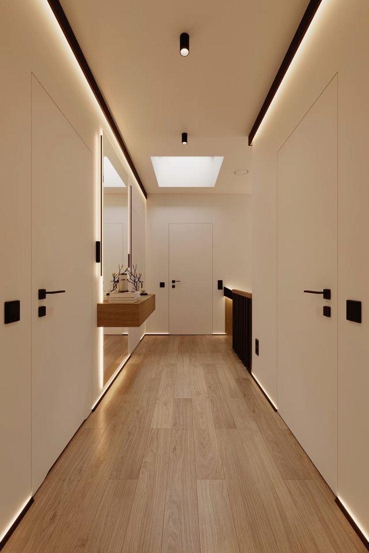 Nowoczesny korytarz z białymi ścianami, drewnianą podłogą, oświetleniem LED wzdłuż sufitu i podłogi, oraz minimalistyczną konsolą z dekoracjami.