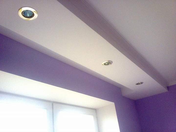 Fioletowa ściana z oknem i białym sufitem podwieszanym z trzema okrągłymi lampami halogenowymi.