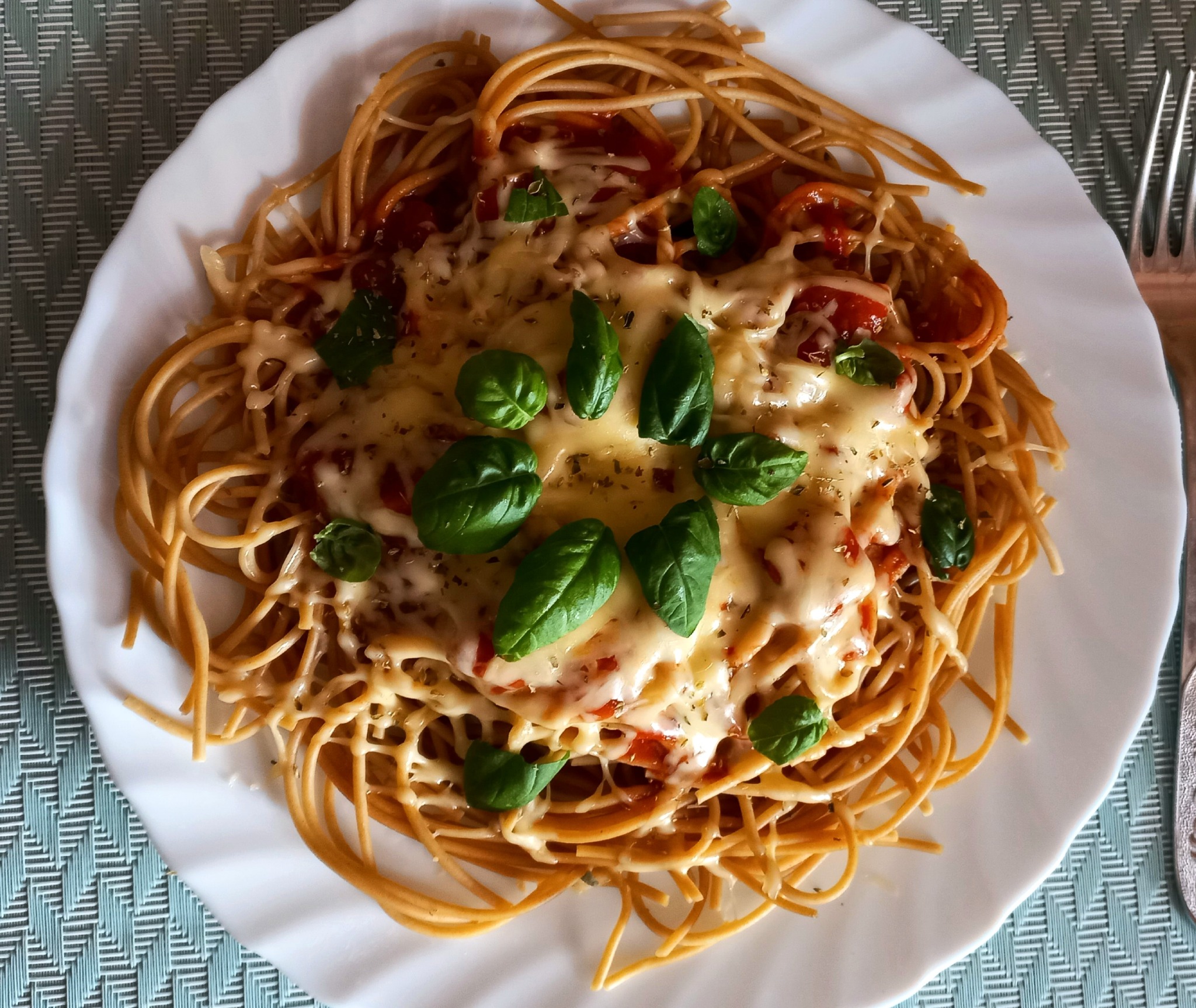Spaghetti z sosem pomidorowym, serem mozzarella i świeżą bazylią na białym talerzu, widok z góry.