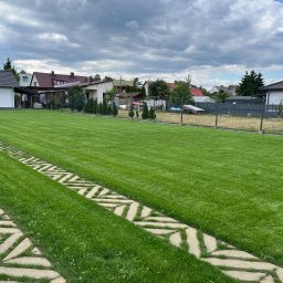 Green Home Łukasz Ogiejko - Idealnie skoszony trawnik z geometrycznym wzorem ścieżki z płyt betonowych, otoczony zielenią i zabudową jednorodzinną w tle, pod pochmurnym niebem.