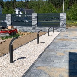 IWOPOWER Ivan Popynchuk - Nowoczesne ogrodzenie panelowe z szarej kostki łupanej i poziomych, metalowych przęseł, uzupełnione ścieżką z białego grysu i niskimi lampami w kształcie łuku, widoczne materiały budowlane przed...