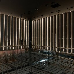 IWOPOWER Ivan Popynchuk - Montaż pionowego oświetlenia LED na ścianie w dużej sali, widoczne rusztowania i pracownicy w oddali.