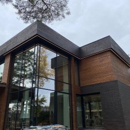 IWOPOWER Ivan Popynchuk - Nowoczesny dom z drewnianą elewacją i dużymi oknami, podświetlony ledami, pracownik na drabinie przy ścianie.