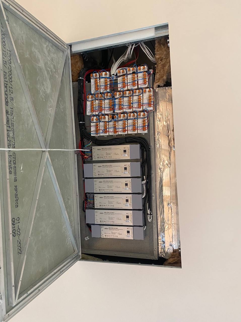 Otwarty panel dostępowy ukazuje zamontowane transformatory i okablowanie, widoczne izolacje i perforowana płyta montażowa.