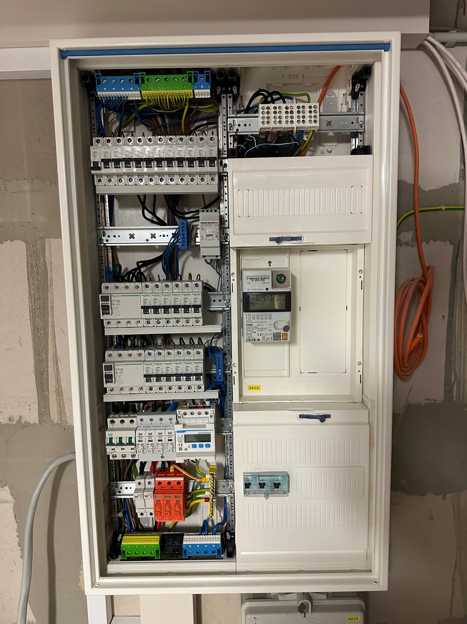 Otwarta skrzynka rozdzielcza z zabezpieczeniami, licznikiem energii elektrycznej i okablowaniem w surowym wnętrzu w Poznaniu. Widoczne bezpieczniki, przewody w różnych kolorach oraz elementy...