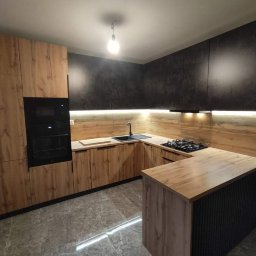 Meble Gutek - Nowoczesna kuchnia na wymiar z drewnianymi frontami szafek dolnych i czarnymi szafkami górnymi, oświetleniem LED podszafkowym i wyspą kuchenną z czarnymi żłobieniami.