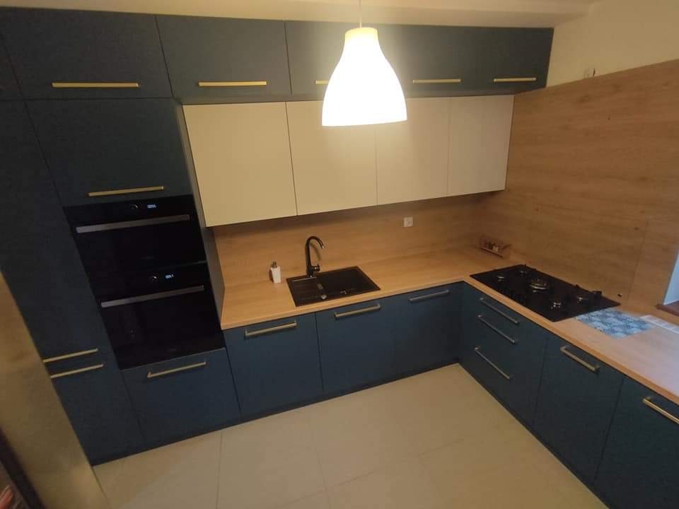 Nowoczesna kuchnia z ciemnoniebieskimi szafkami, drewnianym blatem i białymi górnymi szafkami, oświetlona wiszącą lampą