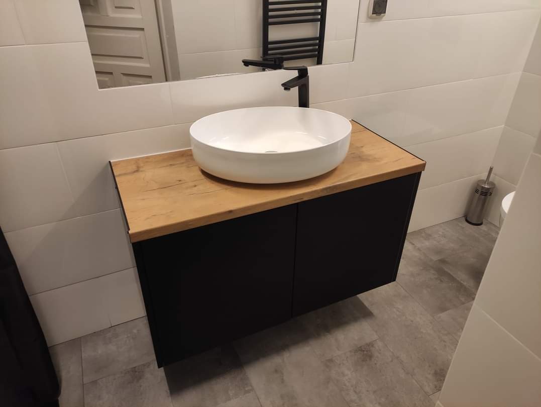 Nowoczesna łazienka z szafką pod umywalkę w kolorze czarnym z blatem drewnopodobnym i okrągłą białą umywalką nablatową.