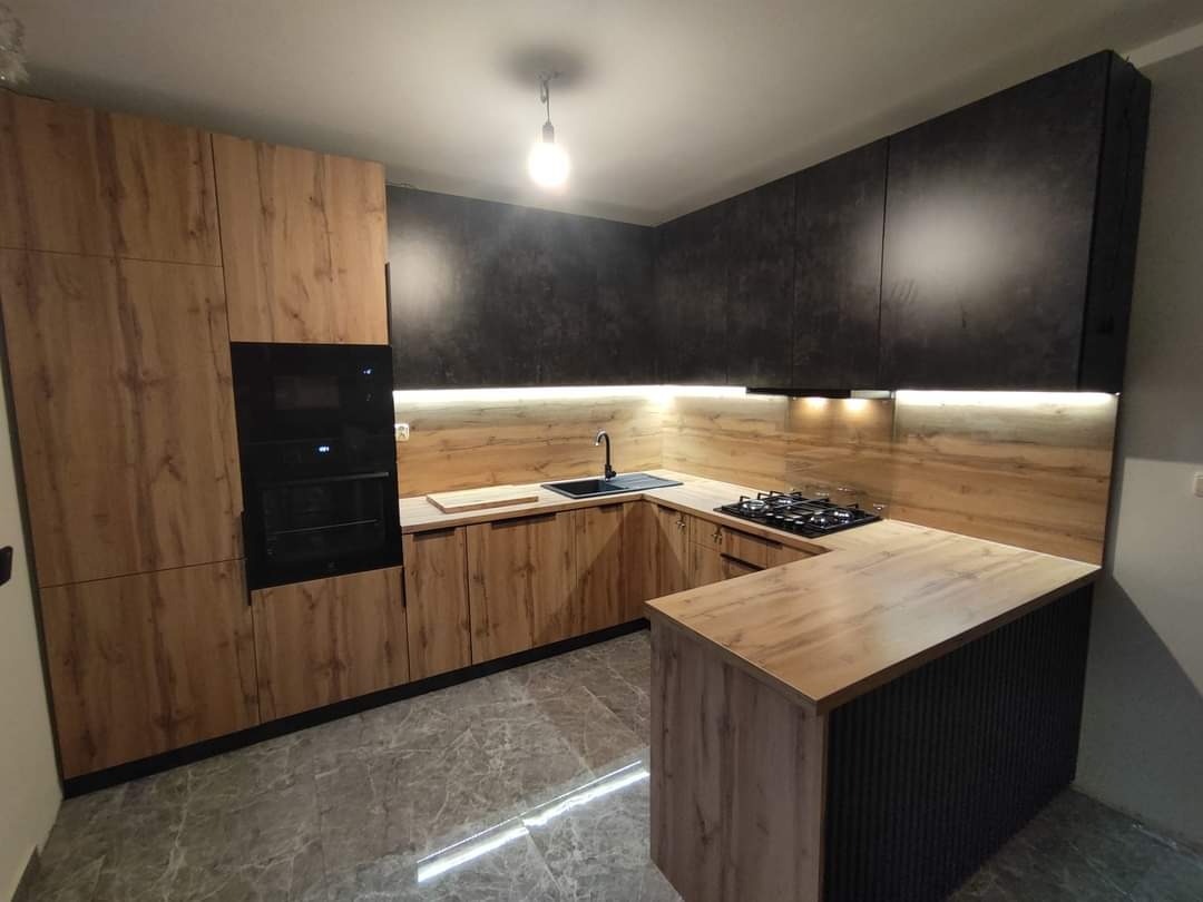 Nowoczesna kuchnia na wymiar z drewnianymi frontami szafek dolnych i czarnymi szafkami górnymi, oświetleniem LED podszafkowym i wyspą kuchenną z czarnymi żłobieniami.