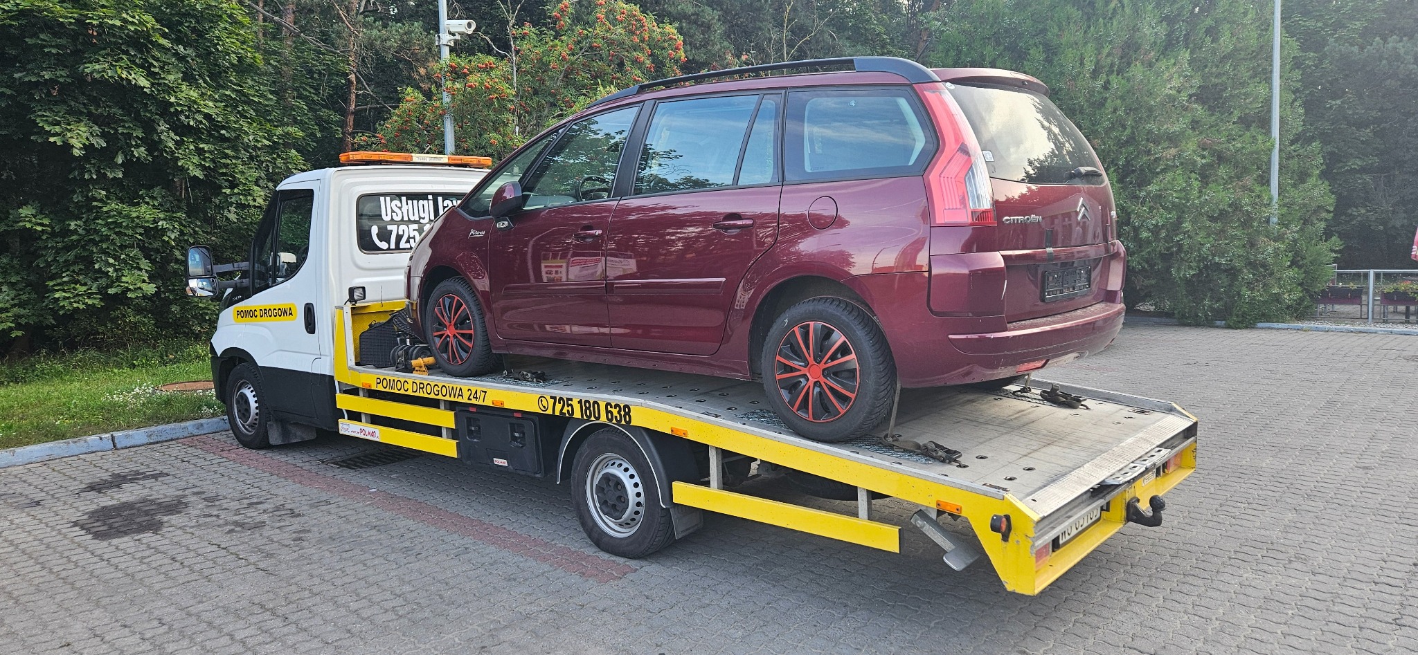 Czerwony Citroen Picasso z felgami z czerwonym akcentem transportowany na żółtej lawecie pomocy drogowej z widocznym numerem telefonu.