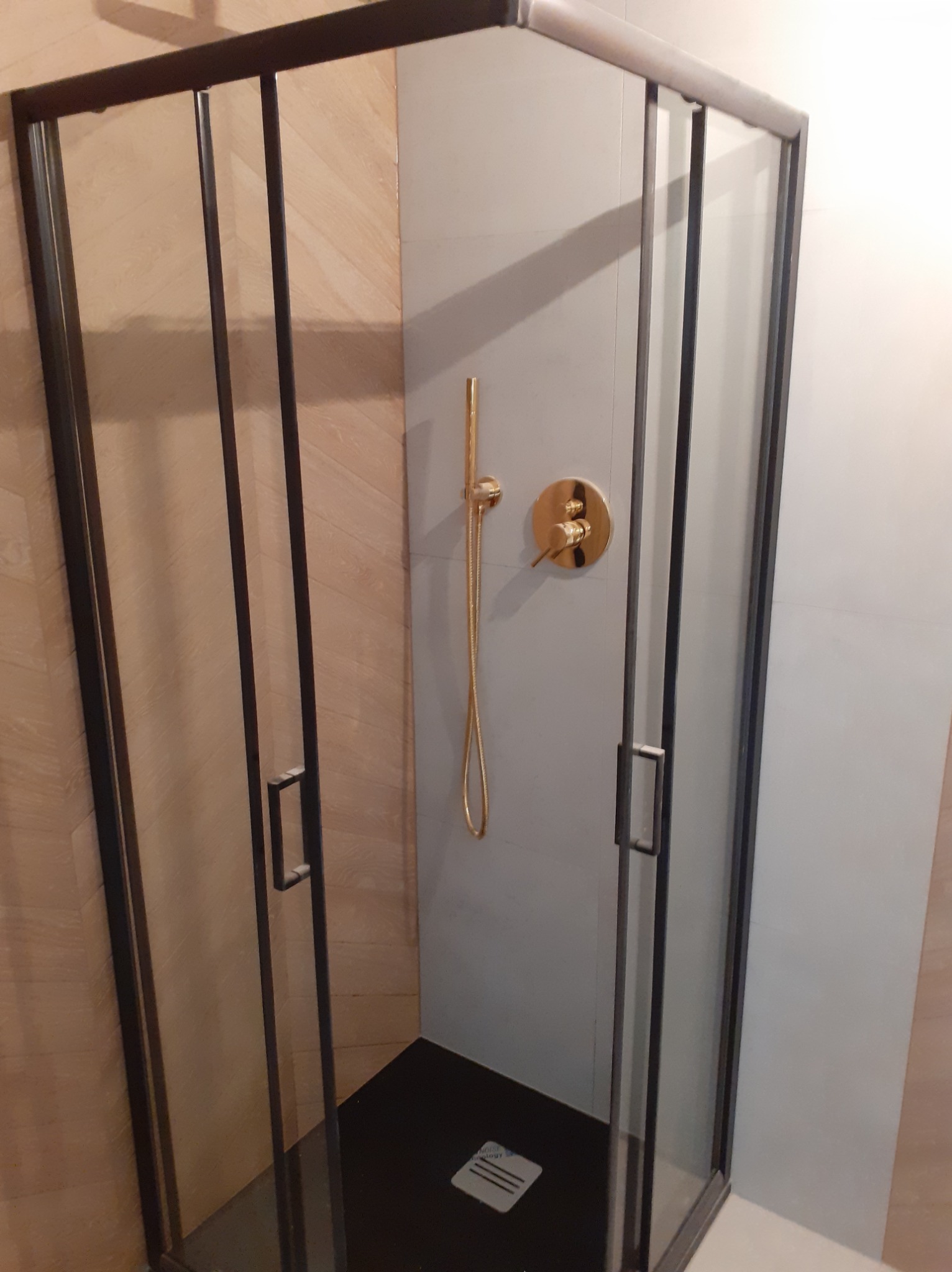 Nowoczesna kabina prysznicowa z czarnymi ramami, złotą armaturą i panelami imitującymi drewno, po remoncie łazienki.