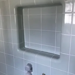 Świeżo położone, jasnoniebieskie płytki ceramiczne w łazience z wnęką na kosmetyki i przygotowanym miejscem na baterię, zabezpieczonym szarą folią ochronną.