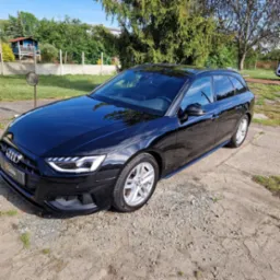 Błyszczący, czarny samochód Audi kombi po umyciu, zaparkowany na żwirowym podłożu w słoneczny dzień.