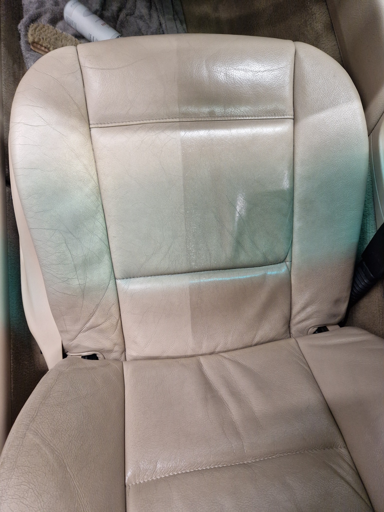 Beżowe skórzane siedzenie samochodowe w trakcie czyszczenia, widoczna różnica między wyczyszczoną a zabrudzoną częścią, obok szczotka i preparat.