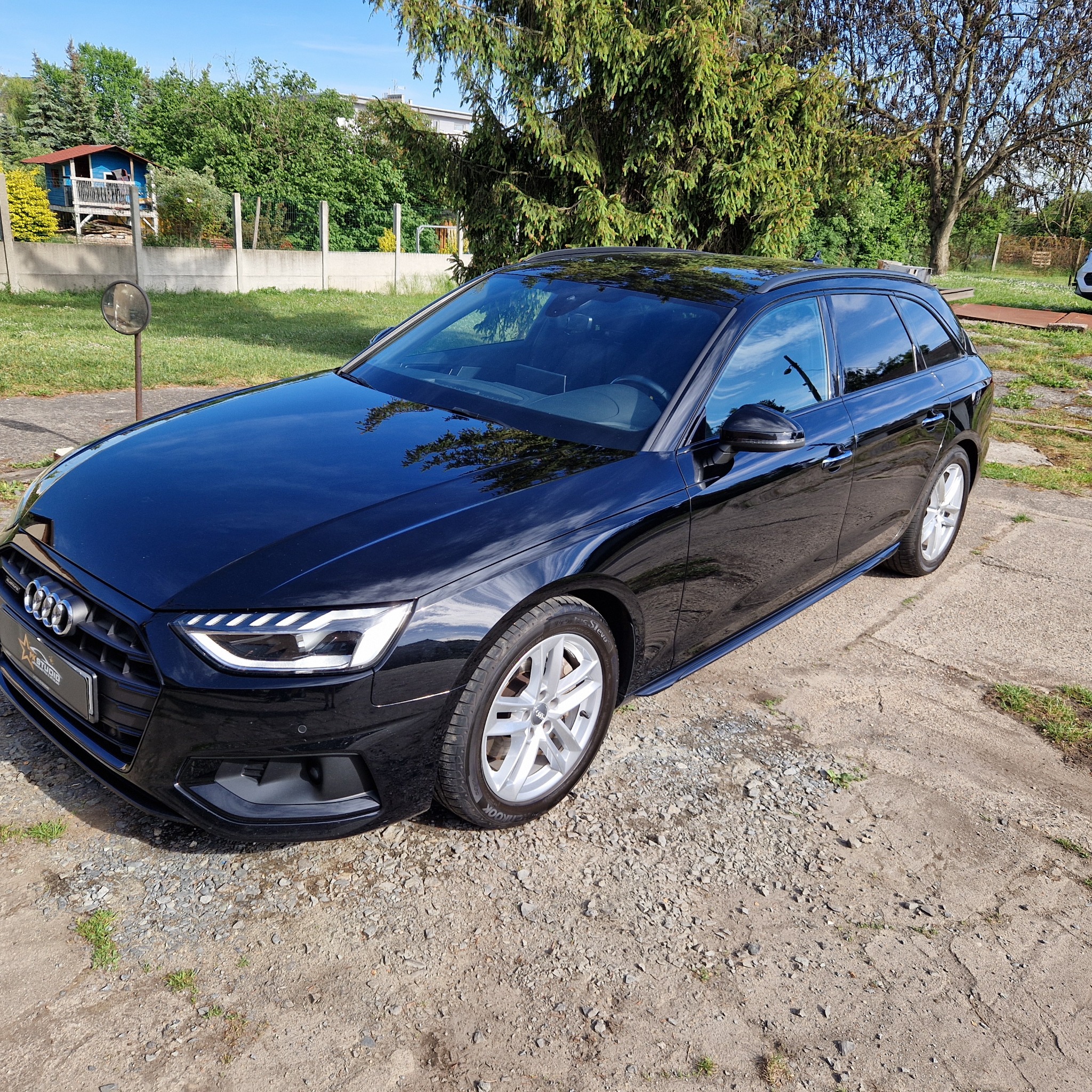 Błyszczący, czarny samochód Audi kombi po umyciu, zaparkowany na żwirowym podłożu w słoneczny dzień.