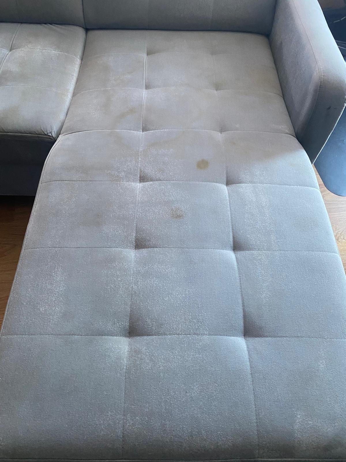 Szara, modułowa kanapa z widocznymi plamami i zabrudzeniami na siedzisku i oparciu, prezentująca potrzebę czyszczenia tapicerki.