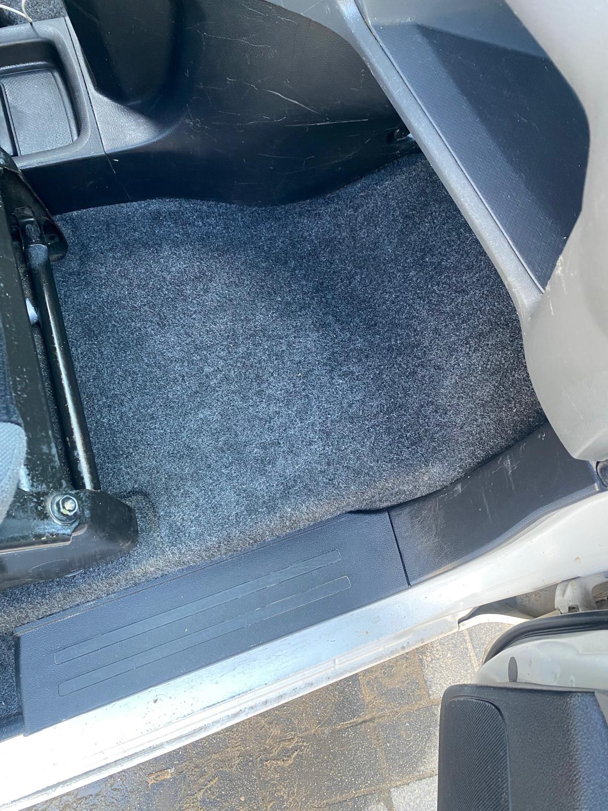 Szara wykładzina podłogowa w samochodzie, widoczny fragment fotela i progu.