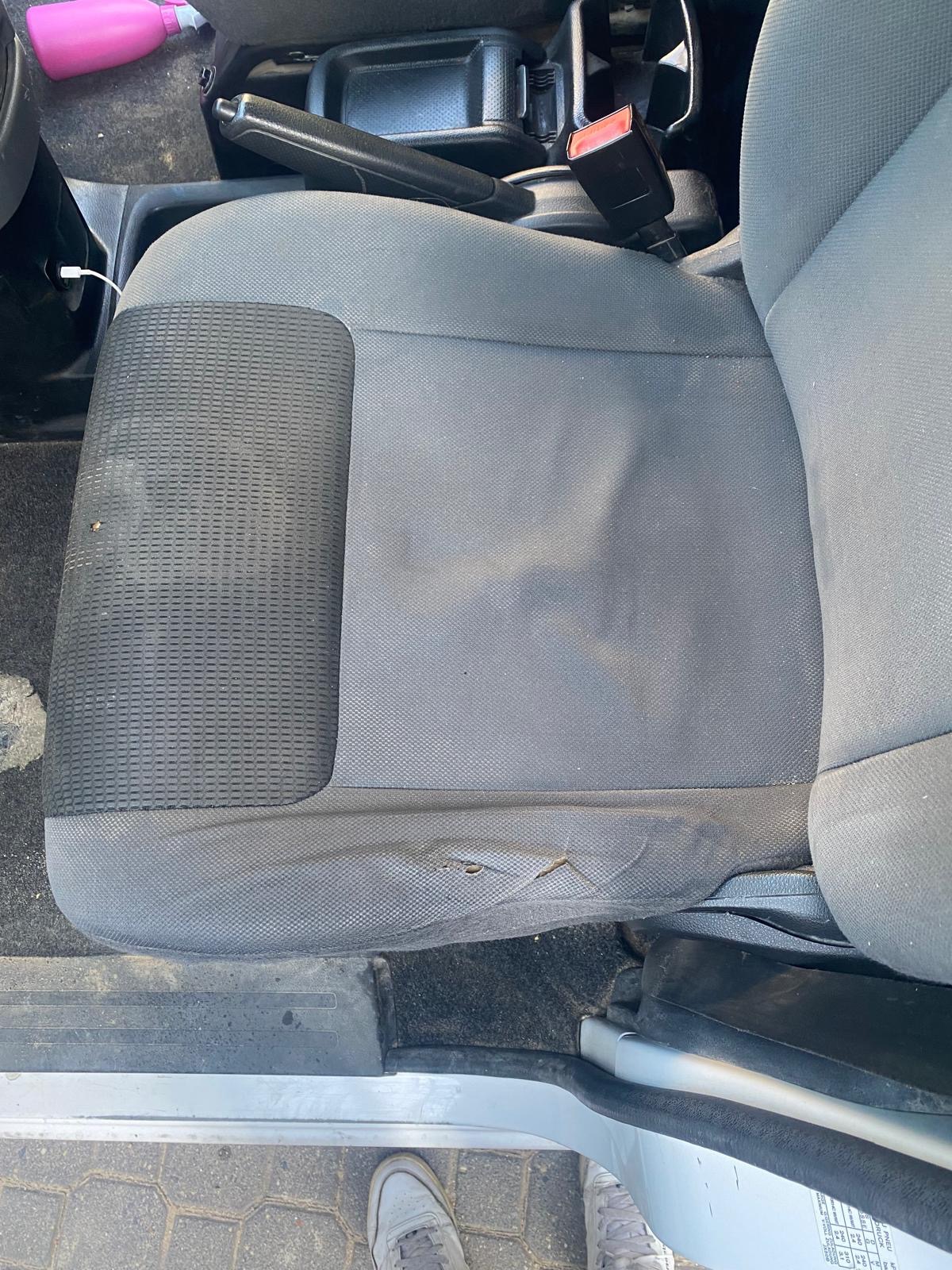 Szare, zabrudzone siedzenie samochodowe z widocznymi plamami i niewielkim uszkodzeniem tapicerki, sfotografowane z góry.