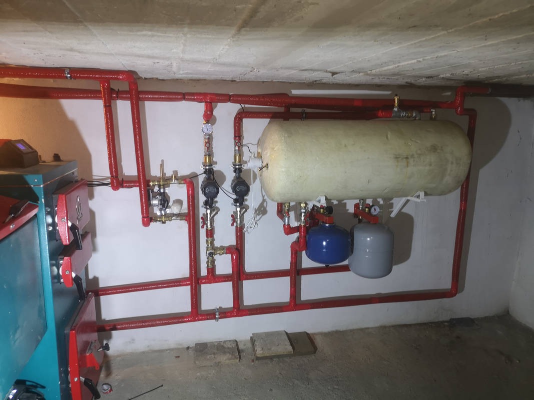 Kotłownia z nową instalacją grzewczą: piec na paliwo stałe, zbiornik akumulacyjny, naczynia przeponowe. Rury w izolacji termicznej, pompy obiegowe z zaworami. Widoczne manometry i automatyka.